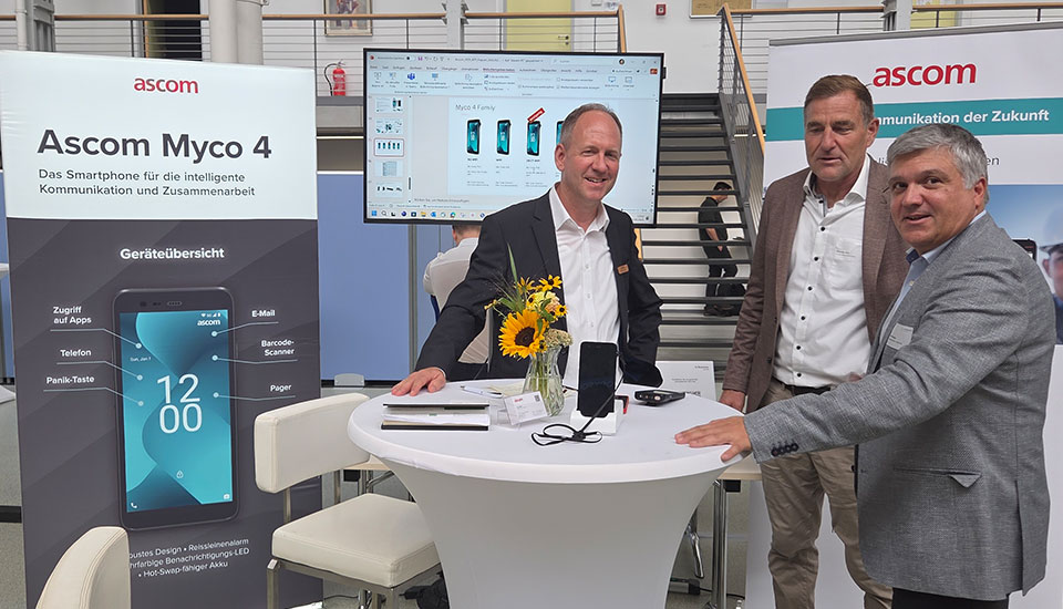 Stand von Ascom auf der 5G-Fachtagung: Drei Unternehmensvertreter präsentieren das Smartphone Ascom Myco 4 für sichere Kommunikation und Zusammenarbeit.
