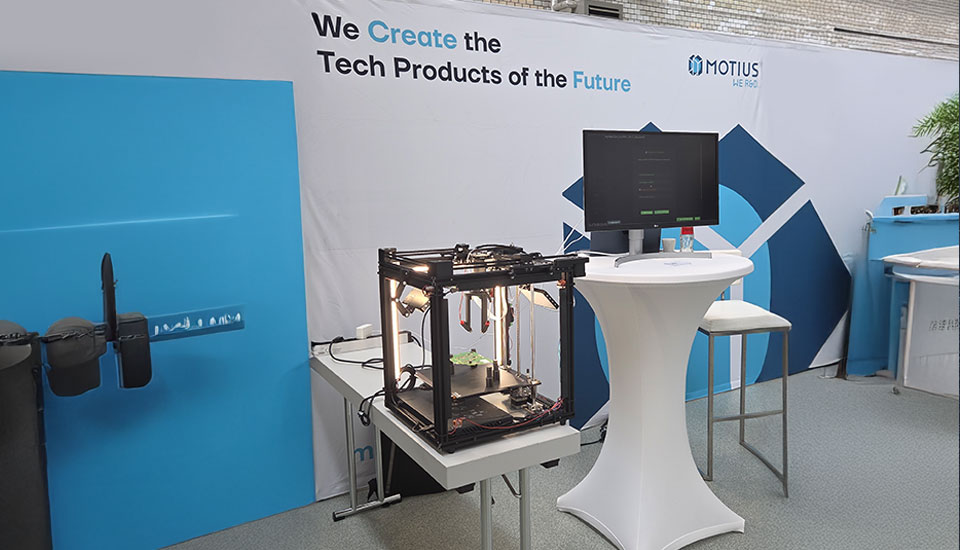 Stand von Motius auf der 5G-Fachtagung mit 3D-Drucker, Monitor und Infowand zu Tech-Produkten der Zukunft.