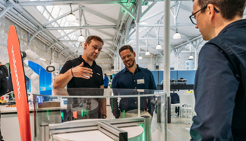 Stand von Valantic auf der 5G-Fachtagung: Mitarbeitende erklären Besuchern ein Qualitätssicherungssystem mit Kamera- und Automatisierungstechnik.