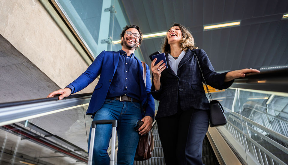 Zwei Geschäftsreisende auf einer Rolltreppe in einem Gebäude – dank Indoor-Mobilfunk jederzeit verbunden