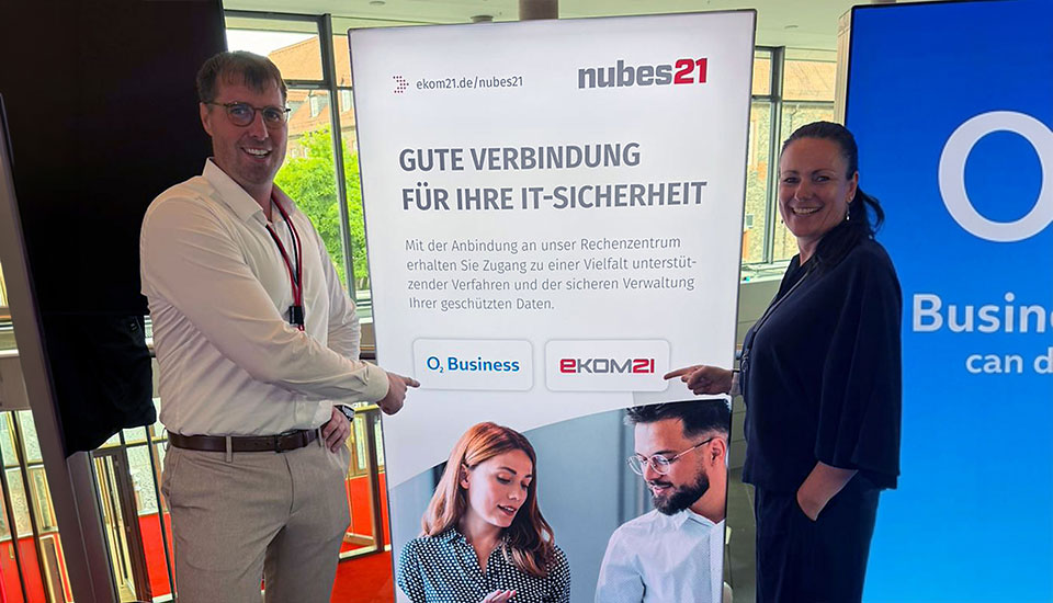 Zwei Personen vor einem Roll-up mit den Logos von o2 Business und ekom21 am gemeinsamen Stand der eXPO26.