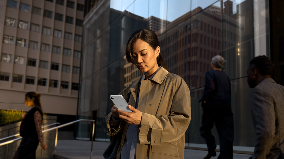 Eine Person nutzt ein iPhone 17e in Weiß, um außerhalb eines Bürogebäudes weiterzuarbeiten