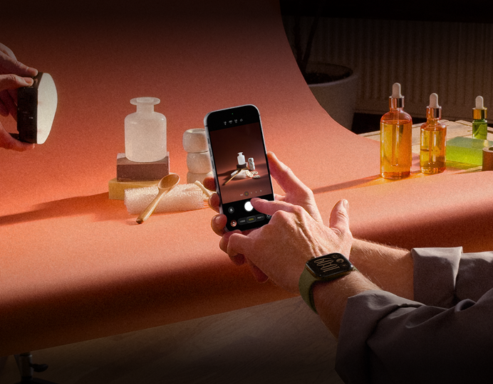 Ein Fotoshooting an einem Arbeitsplatz, eine Person fotografiert mit einem iPhone Produkte vor einem Hintergrund, eine Person hält eine Lampe