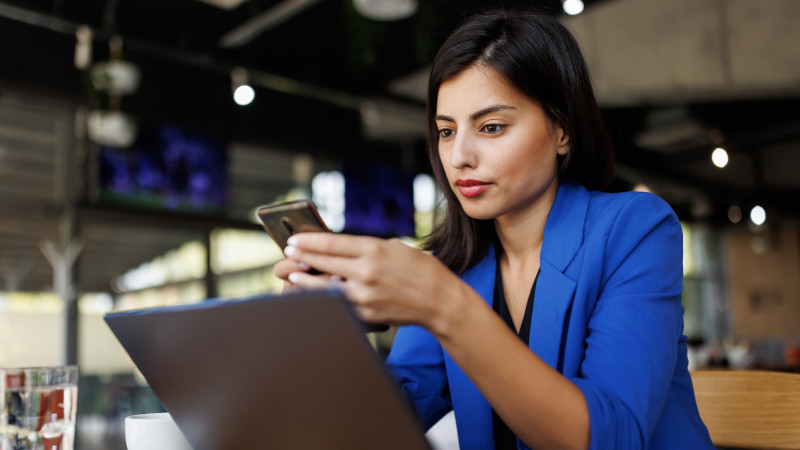 Moderne Geschäftsfrau mit Handy und Laptop bei der Arbeit