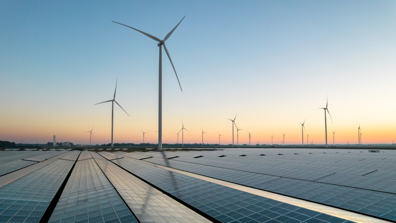 Wind- und Solarkraftanlagen im Sonnenaufgang vor der Skyline einer Stadt