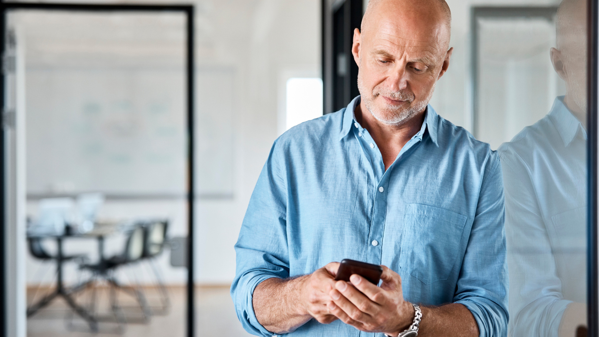 Ein älterer Mitarbeiter nutzt sein Smartphone im Büro