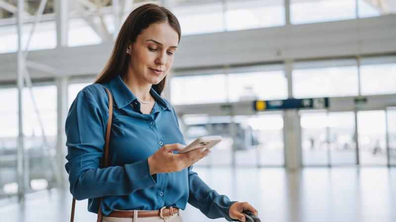 Eine Geschäftsfrau schaut am Flughafen auf ihr Smartphone.