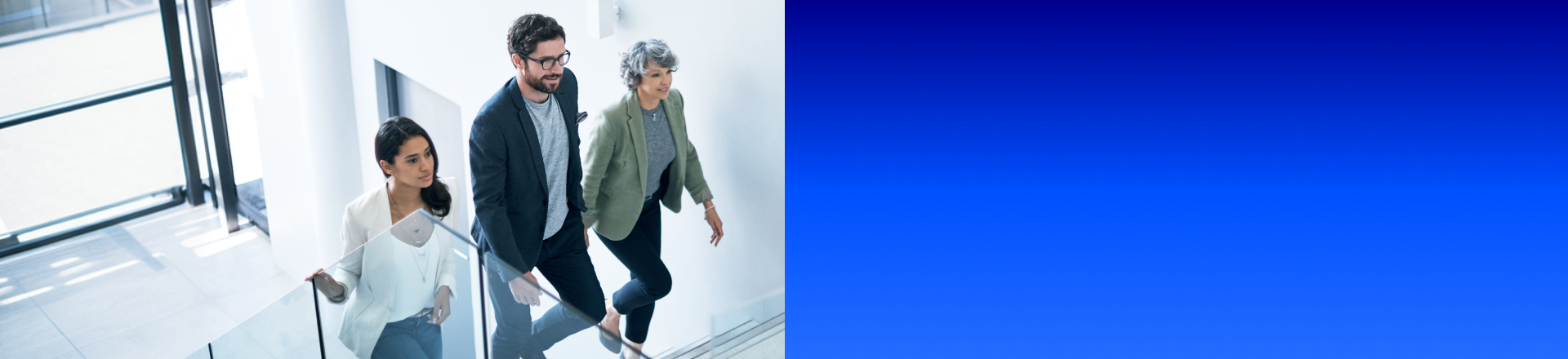 Gruppe von drei Personen geht gemeinsam eine moderne Treppe in einem hellen Bürogebäude hinauf.