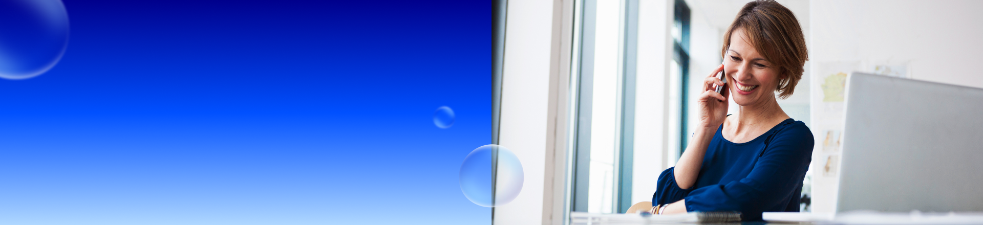 Abbildung: Eine Frau sitzt lächelnd am Schreibtisch und telefoniert.