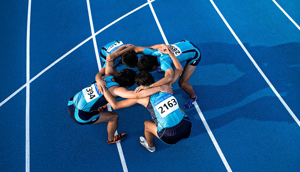 Vier Athleten stehen im Kreis und legen die Arme umeinander, um sich vor dem Start gegenseitig zu motivieren.