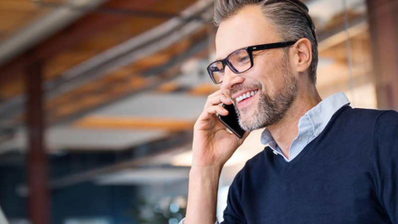 Abbildung: Mann mit Bart und Brille hält Handy ans Ohr und lächelt