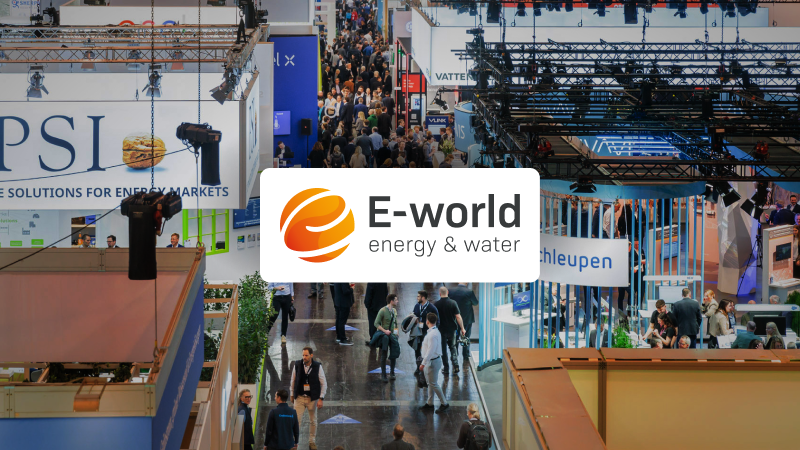 Blick auf eine große Messehalle mit vielen Menschen, Ständen und Bannern. Im Vordergrund das Logo ‚E-world energy & water‘ mit orangefarbenem Globus-Symbol.